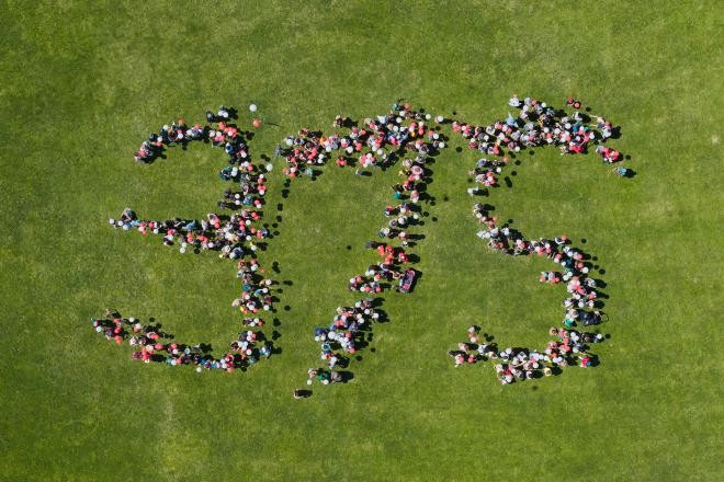 Zahlreiche Menschen bilden stehend auf einer Wiese die Zahl 375