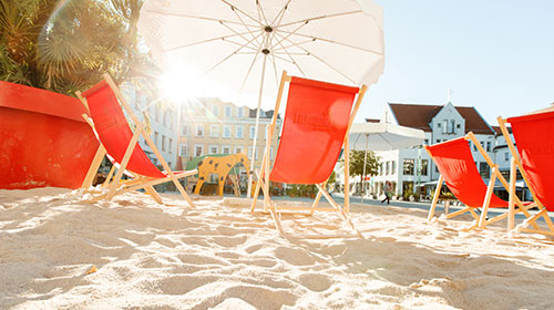 Rote Liegestühle auf Sand vor dem Rathaus