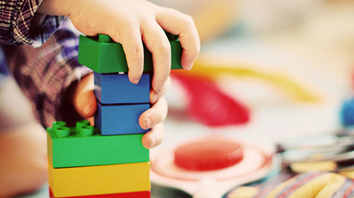 Kinderhände stapeln Klemmbausteine übereinander zu einem Turm.