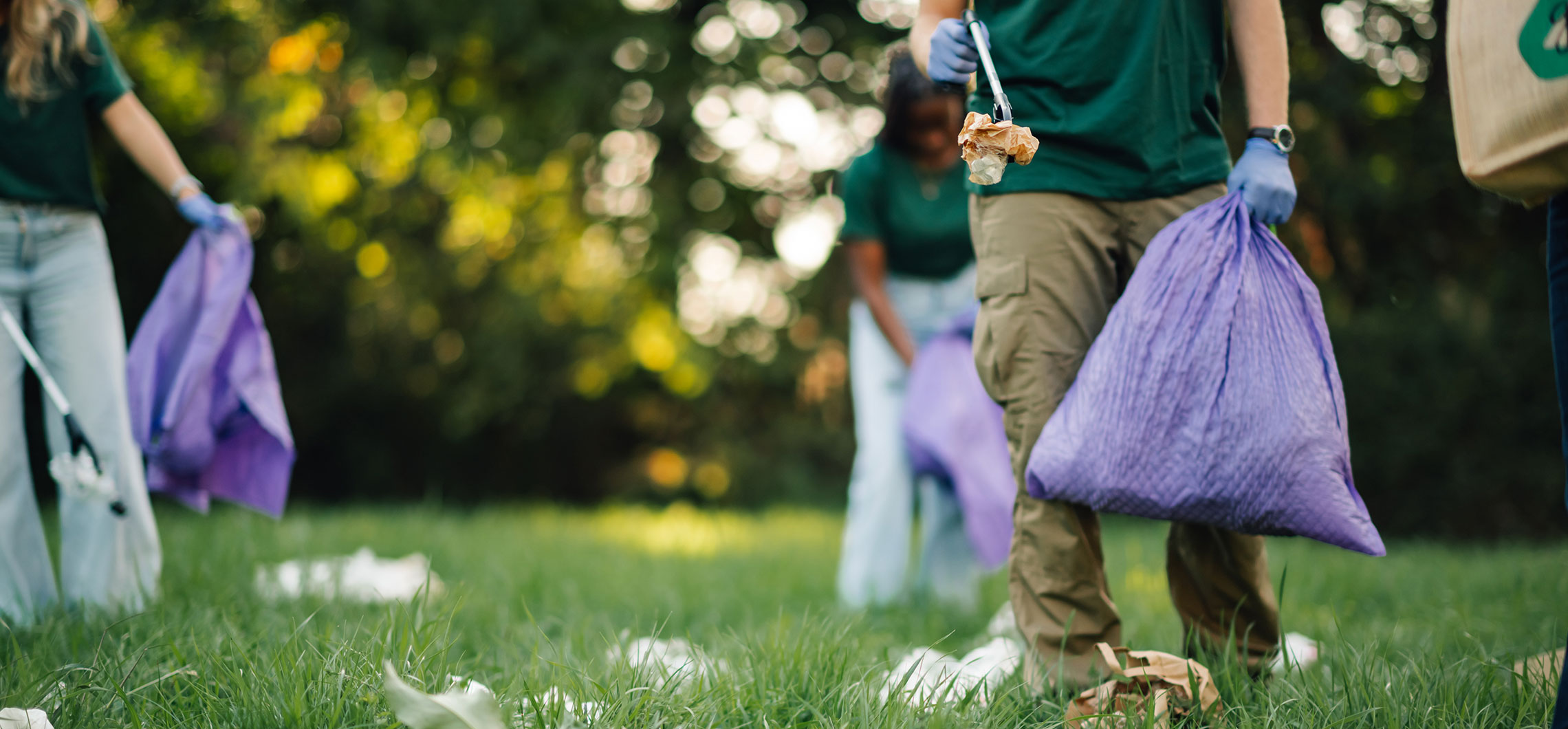 Mehrere Menschen laufen durch eine Grünanlage und sammeln mit Greifhaken Müll ein.