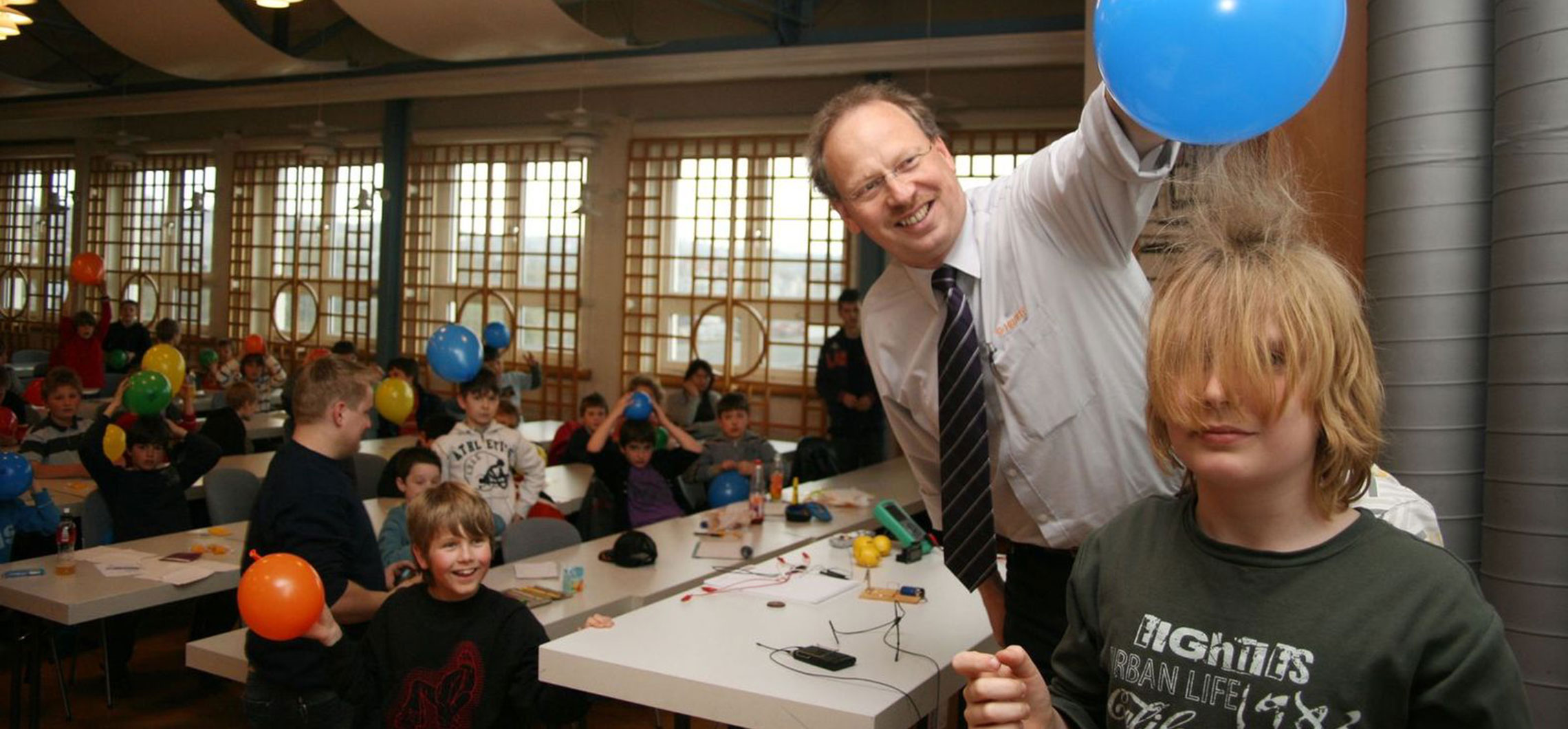 Einblick in die Kinderuni in Göppingen. Ein Dozent hält einen Luftballon über dem Kopf eines Kindes.