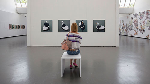 Eine Frau sitzt in der Kunsthalle in Göppingen mittig im Bild auf einem Stuhl und betrachtet ein Bild.