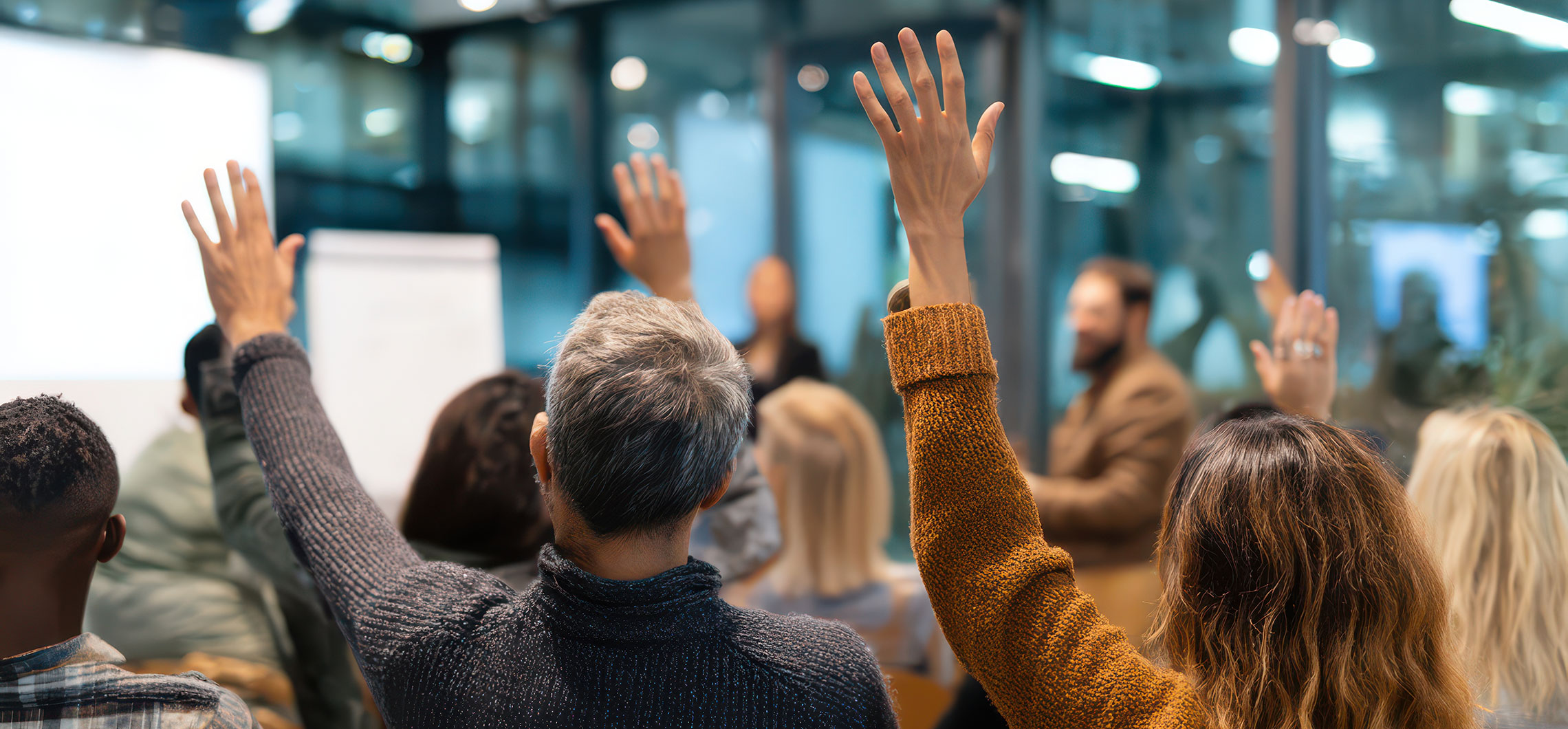 Eine Gruppe von Menschen in einem Besprechungsraum, mehrere Hände sind erhoben