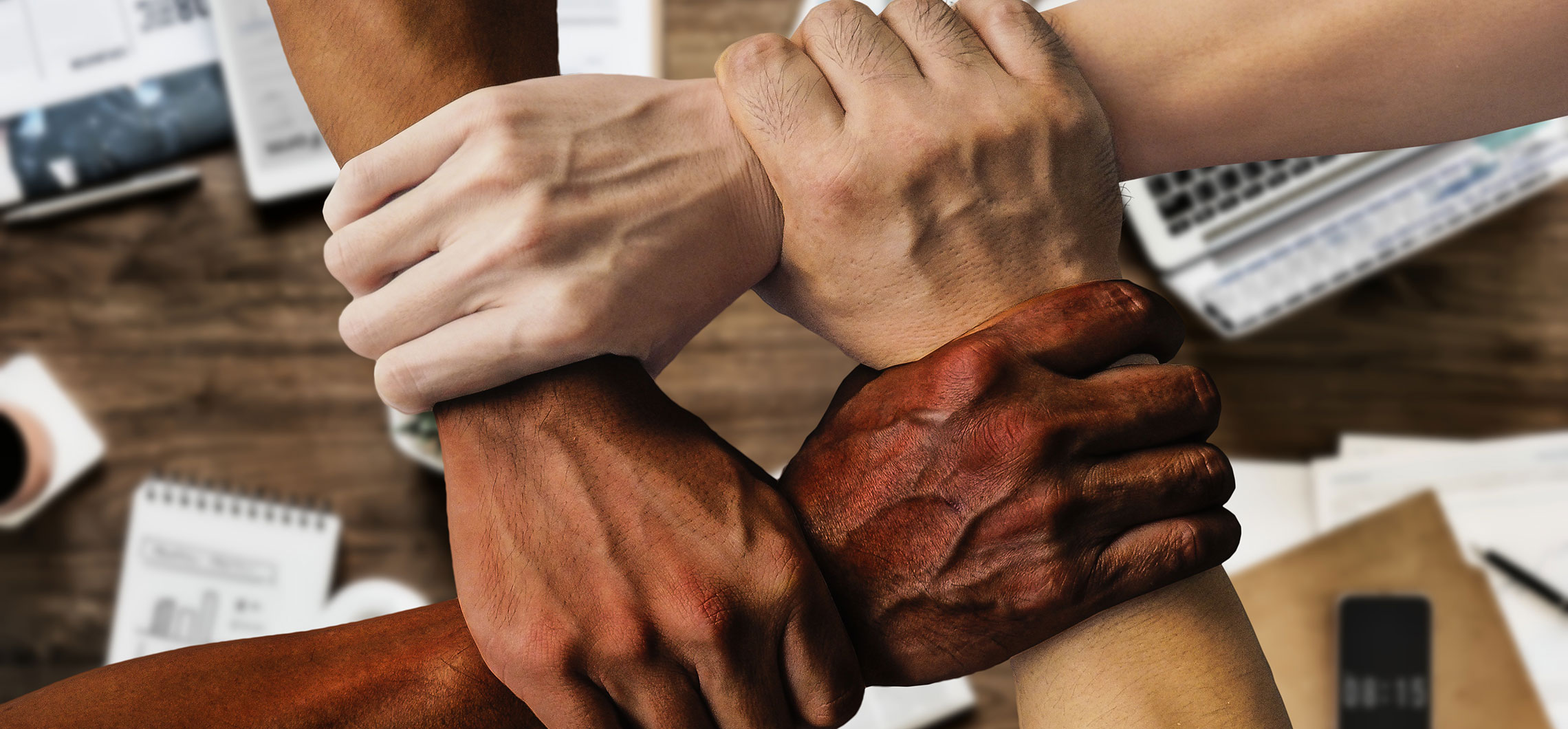 Menschen mit unterschiedlicher Hautfarbe halten sich einander an den Handgelenken