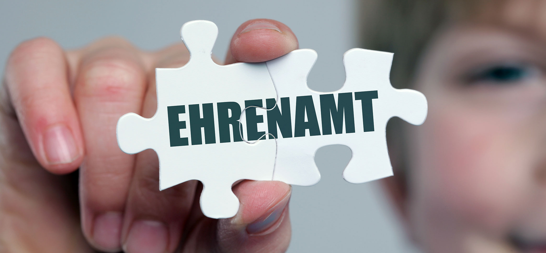 Ein Person hält zwei zusammengefügte Puzzlestücke vor die Kamera. Darauf steht Ehrenamt.