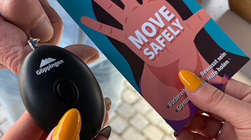 Eine Frau hält einen Flyer und einen Taschenalarm in der Hand