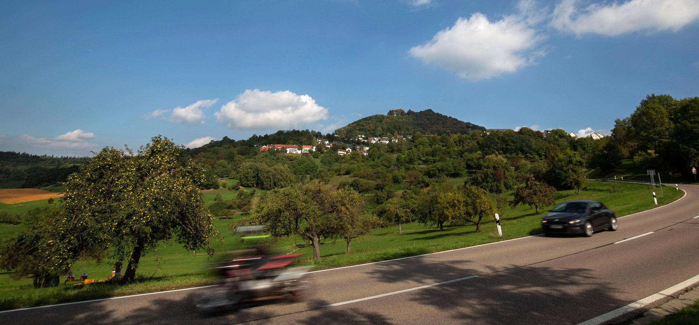 Ein Foto des Bergs und des Dorfes Hohenstaufen. Im Vordergrund ist eine Straße zu sehen.