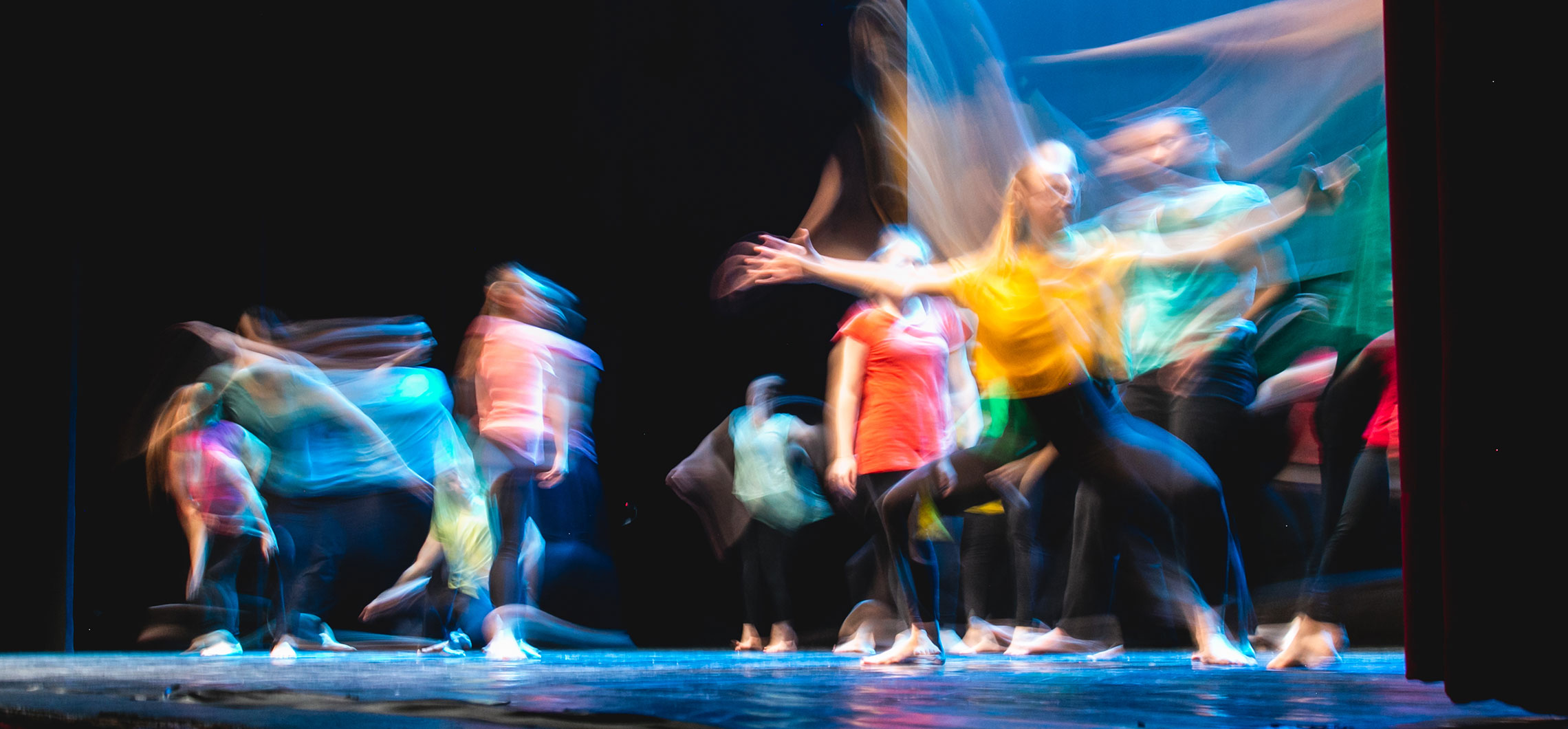Verschwommenes Bild mehrerer junger Menschen, die tanzend auf einer Bühne stehen.
