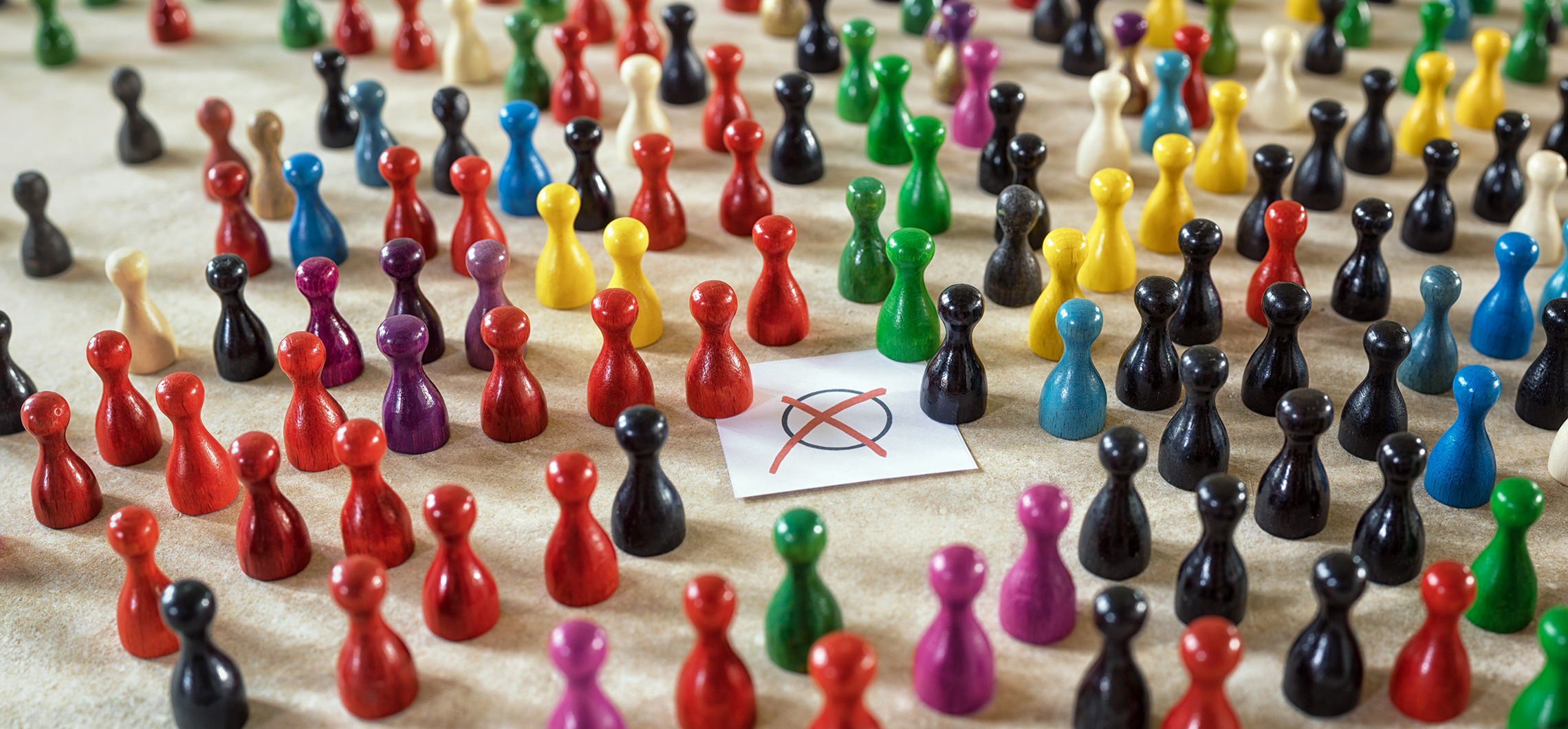 Spielfiguren in unterschiedlichen Farben stehen um ein Blatt Papier, auf dem ein rotes Kreuz abgebildet ist.