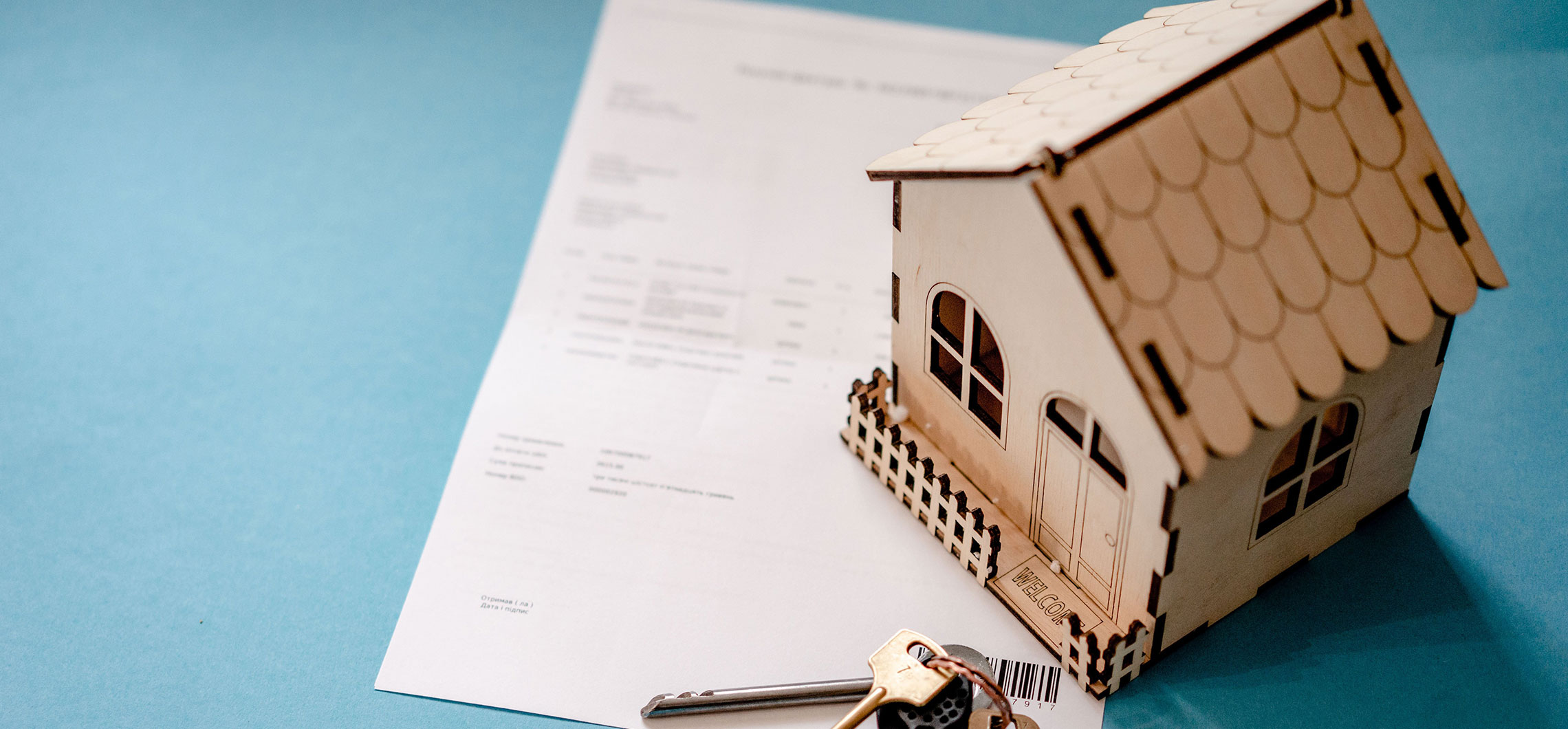 Ein kleines Modellhaus aus Holz, das auf einem symbolischen Vertrag liegt.