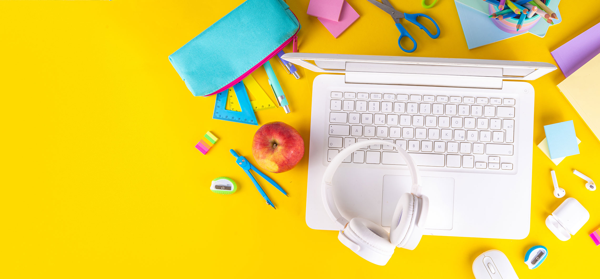 Auf einem gelben Untergrund stehen unter anderem ein Laptop, Kopfhörer und Stifte.
