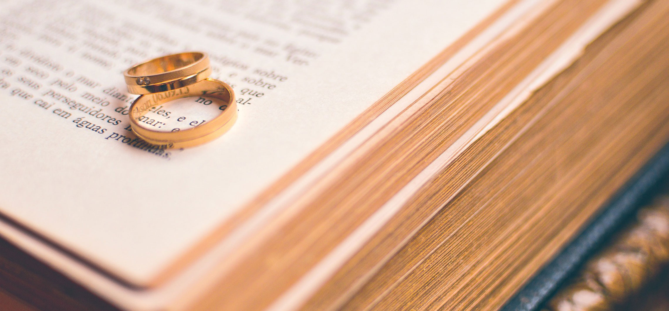 Zwei Eheringe liegen übereinander auf einem historisch anmutenden Buch.