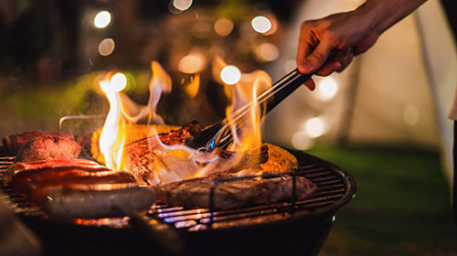 Ein Mann hält eine Grillzange über einen Grill mit Grillgut