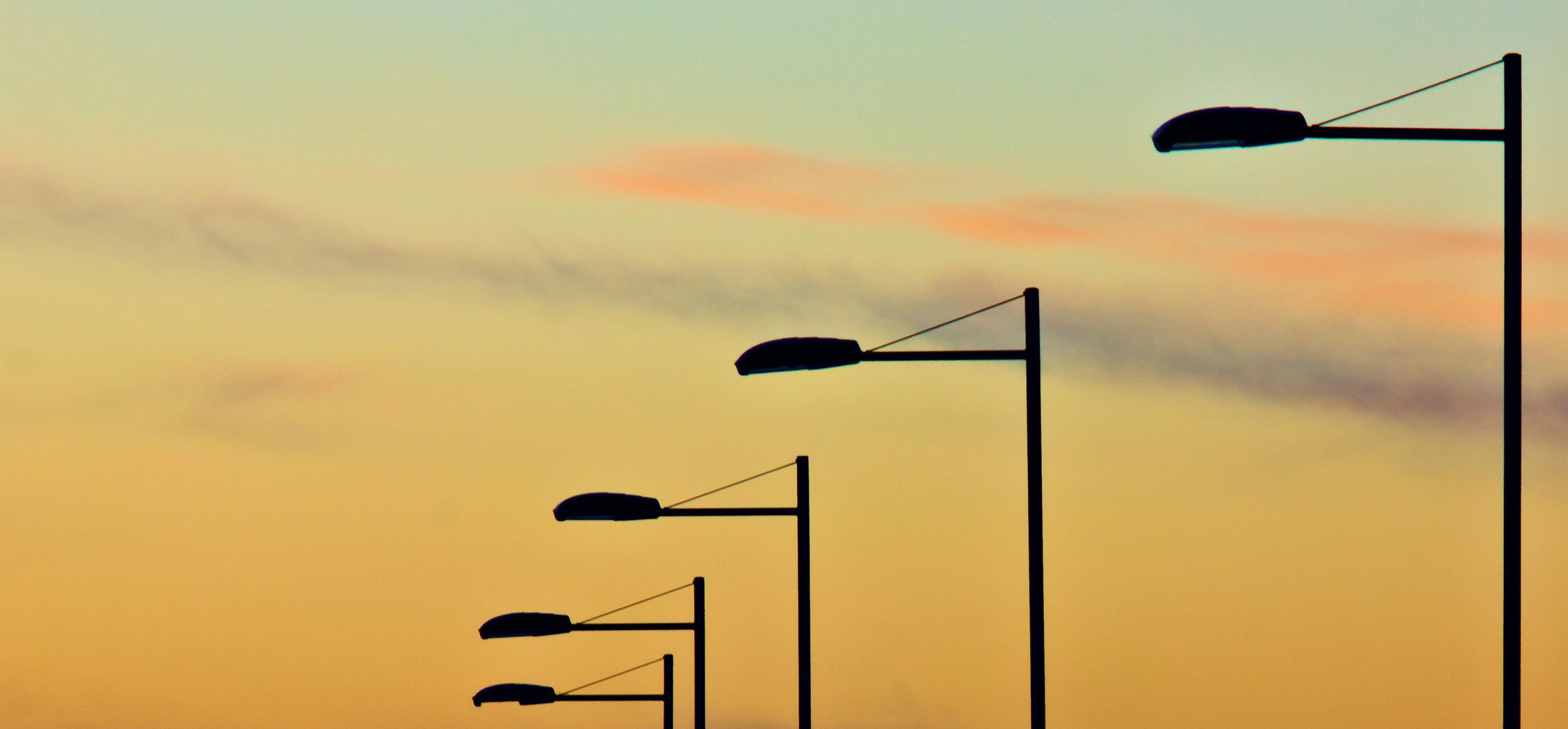 Einzelne Straßenlaternen vor einem orangefarbenen Himmel