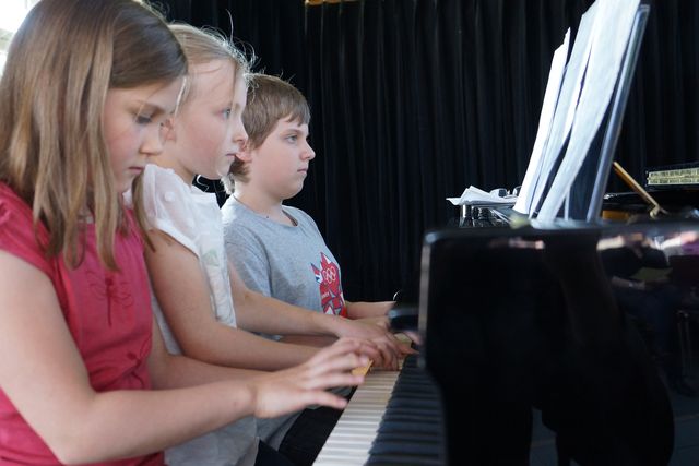 Drei Kinder spielen gemeinsam Klavier.
