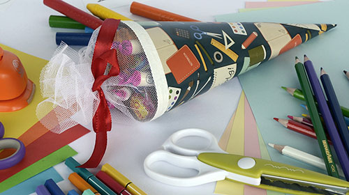Eine Schultüte, eine Schere, buntes Papier und Buntstifte liegen auf einem Tisch.