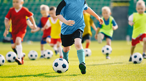 Mehrere Kinder in bunten Trikos spielen Fußball auf einem Rasen