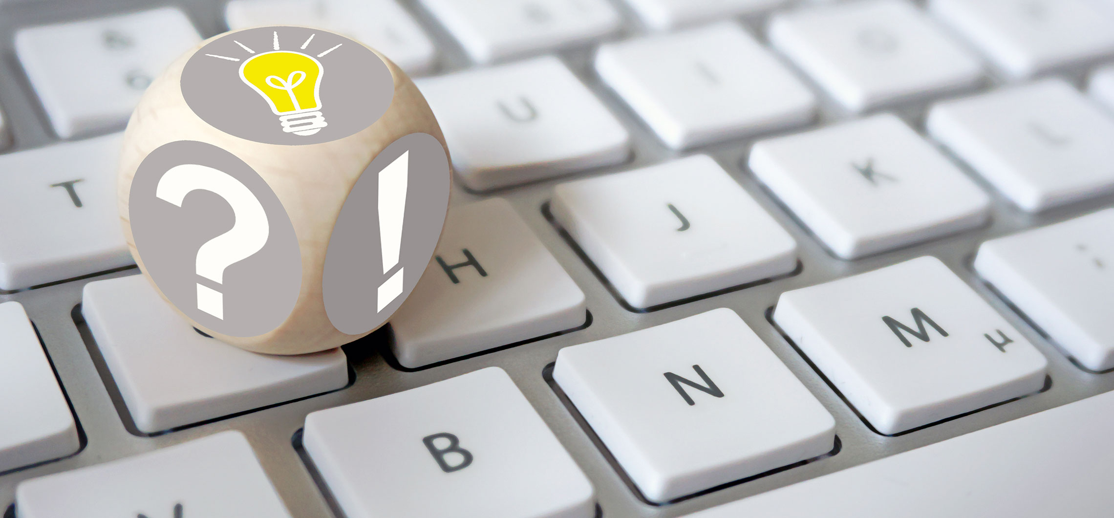 Ein Würfel mit einer Glühbirne, einem Fragezeichen und einem Ausrufezeichen steht auf einer Tastatur.