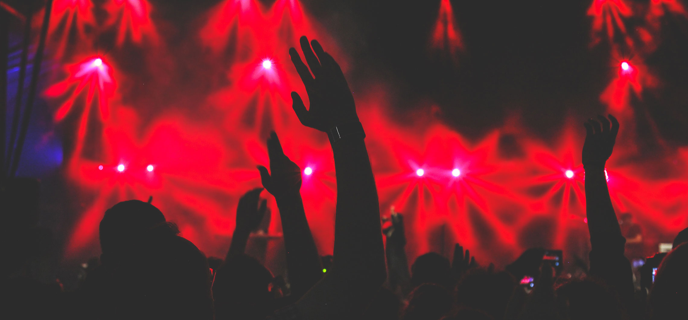 Erhobene Hände während eines Konzerts, im Hintergrund strahlen dunkelrote Lichter