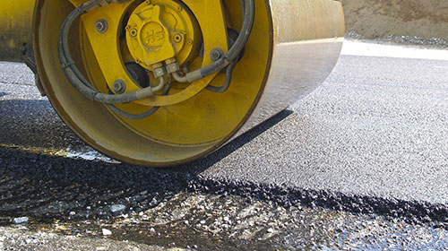 Symbolbild für Straßenarbeiten. Eine Walze fährt über frischen Teer.