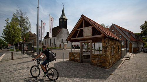 Die Ortsmitte von Bartenbach. Zu sehen sind die Kirche, im Vordergrund fährt jemand mit dem Fahrrad vorbei.